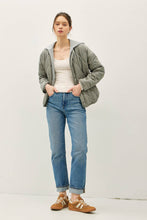 Load image into Gallery viewer, Woman wearing a green jacket, white top, blue jeans, and brown shoes on a white background