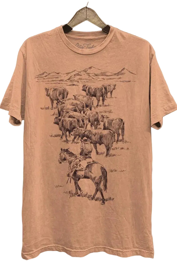 Beige t-shirt with cowboy graphic hanging on a brick wall.