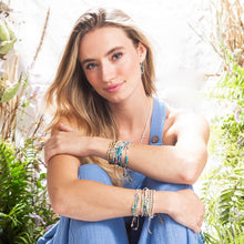 Load image into Gallery viewer, Woman in a blue dress with greenery in the background