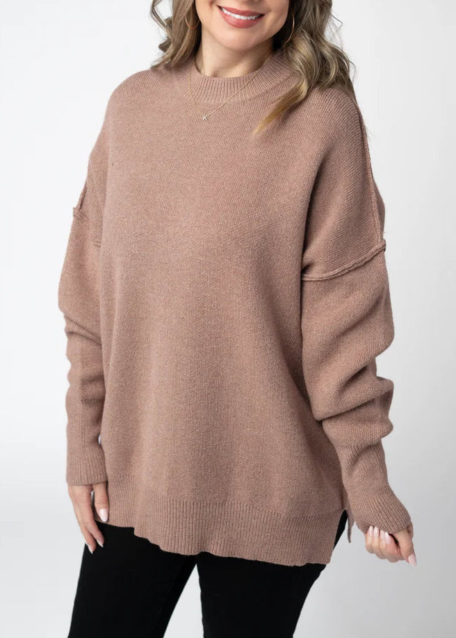 woman wearing light brown long sweater in studio setting with grey background