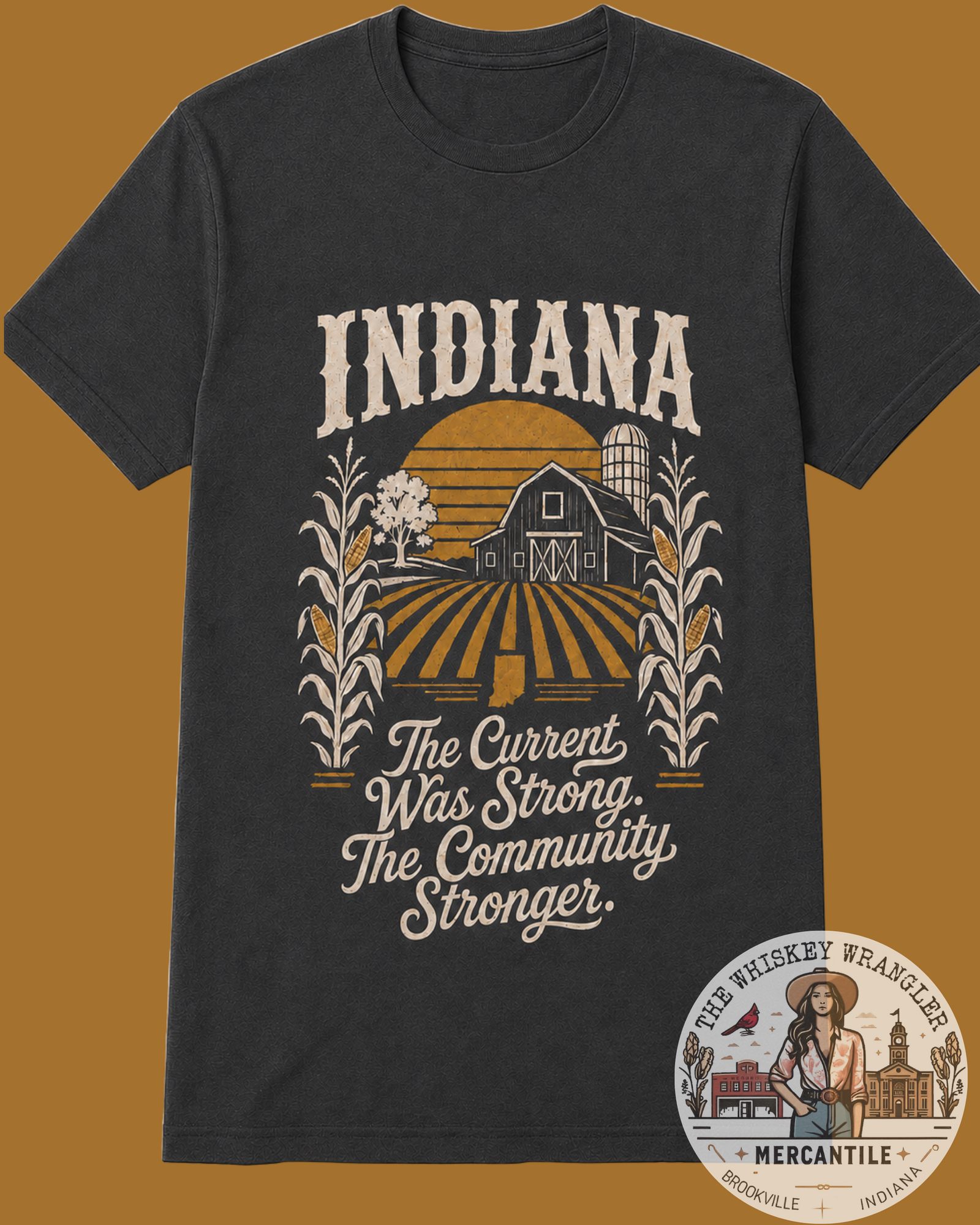 A dark charcoal gray graphic t-shirt displayed flat against a solid mustard brown background. The shirt features a vintage-style Indiana farm illustration with a barn, silo, corn stalks, and a sunset, accompanied by the text 'INDIANA The Current Was Strong.