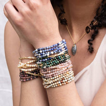 Load image into Gallery viewer, Close-up of a person's arm wearing multiple beaded bracelets on a plain background