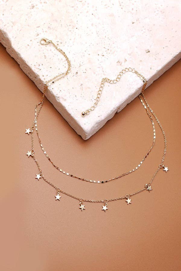 Rose gold necklace with star pendants on a beige stone surface