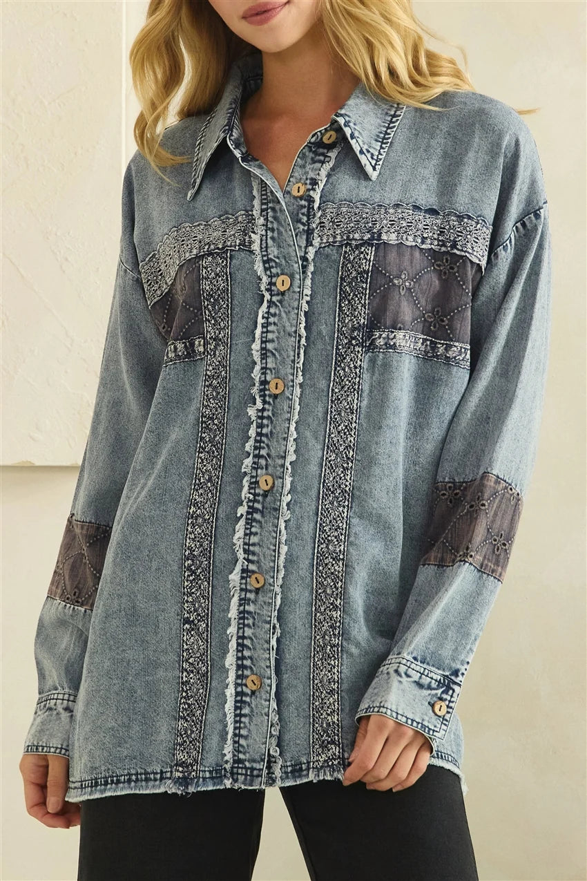 A woman wearing a light blue denim button-up shirt with decorative contrast stitching and dark brown quilted patchwork details on the chest and sleeves, paired with black pants.