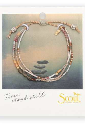 Necklace with stones on a card featuring 'Scout' brand, 'Time stood still' text, and a scenic background.