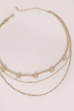 Load image into Gallery viewer, Gold necklace with floral pendants on a light pink background