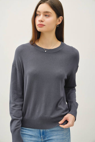 Woman wearing a gray sweater and blue jeans against a white background