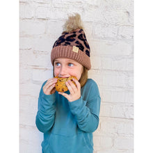 Load image into Gallery viewer, Child wearing a leopard print beanie and blue sweatshirt eating a cookie against a light brick wall.
