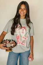 Load image into Gallery viewer, Woman wearing a graphic t-shirt holding a tray with decorative items against a plain background
