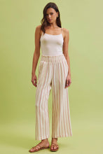 Load image into Gallery viewer, Woman wearing a white top and striped pants on a green background