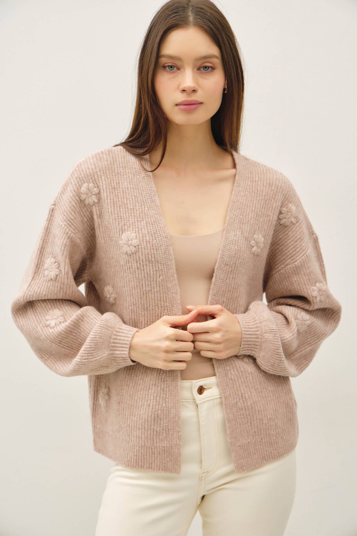 Woman wearing a beige cardigan with floral patterns on a white background