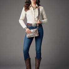 Load image into Gallery viewer, Woman wearing a white blouse, blue jeans, and brown cowboy boots holding a silver clutch against a gray background