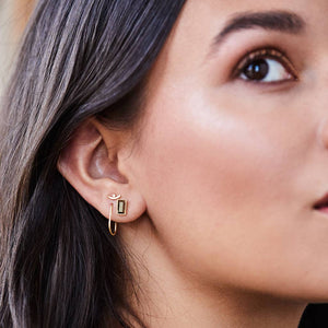 Close-up of a woman wearing a gold earring with a green gemstone.