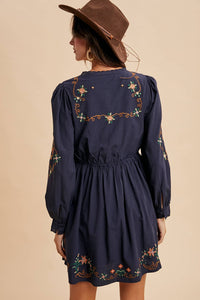 Navy blue dress with floral embroidery worn by a person against a beige background