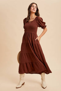 Woman wearing a brown dress with puffed sleeves on a beige background