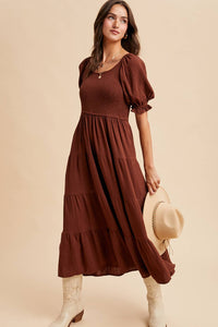 Woman wearing a brown dress holding a hat against a beige background