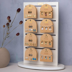 Jewelry display with various earrings on a wooden stand against a gray wall.