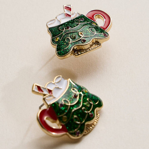 Two green Christmas tree-shaped pins with red bases on a beige background