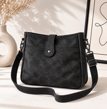 Load image into Gallery viewer, Black crossbody bag on a light surface with a neutral background