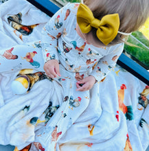 Load image into Gallery viewer, Child wearing a onesie with chicken pattern and a yellow bow, sitting on a surface with more chicken-themed fabric.