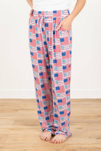 Load image into Gallery viewer, Person wearing red, white, and blue patterned pajama pants on a wooden floor.