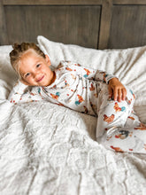 Load image into Gallery viewer, Child wearing a patterned onesie lying on a bed