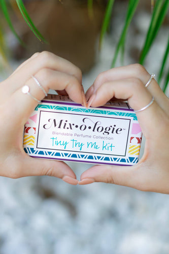 Two hands holding a small tin labeled 'Mixologie' with a blurred natural background
