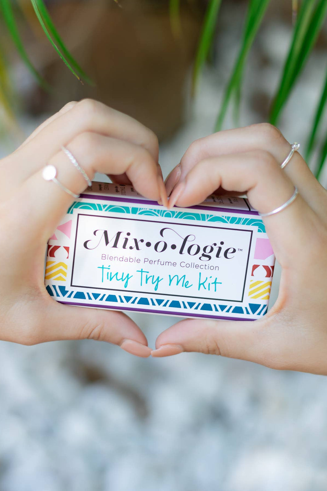 Two hands holding a small tin labeled 'Mixologie' with a blurred natural background