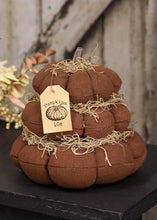 Load image into Gallery viewer, A brown fabric pumpkin-shaped decorative pillow with a small clear stem, wrapped in jute twine and hanging a paper tag that reads 'Pumpkin 10c'. The pillow sits on a black surface with dried flowers and a rustic wooden background.