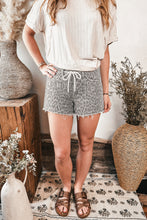 Load image into Gallery viewer, Person wearing a beige top and patterned shorts standing in a room with decorative vases and plants.