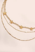 Load image into Gallery viewer, Three gold necklaces with charms on a beige background