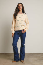 Load image into Gallery viewer, Woman wearing a cream sweater with floral patterns and blue jeans against a plain background