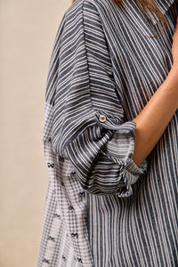 Close-up of a person wearing a black and white striped shirt with rolled-up sleeves against a beige background.