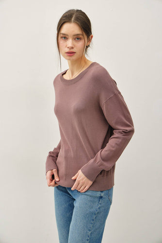 Woman wearing a mauve long-sleeve top and blue jeans on a white background