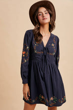 Load image into Gallery viewer, Woman wearing a navy dress with floral embroidery and a brown hat against a beige background
