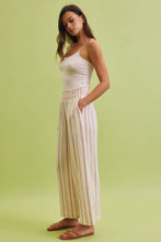 Load image into Gallery viewer, Woman wearing a white top and striped pants on a green background