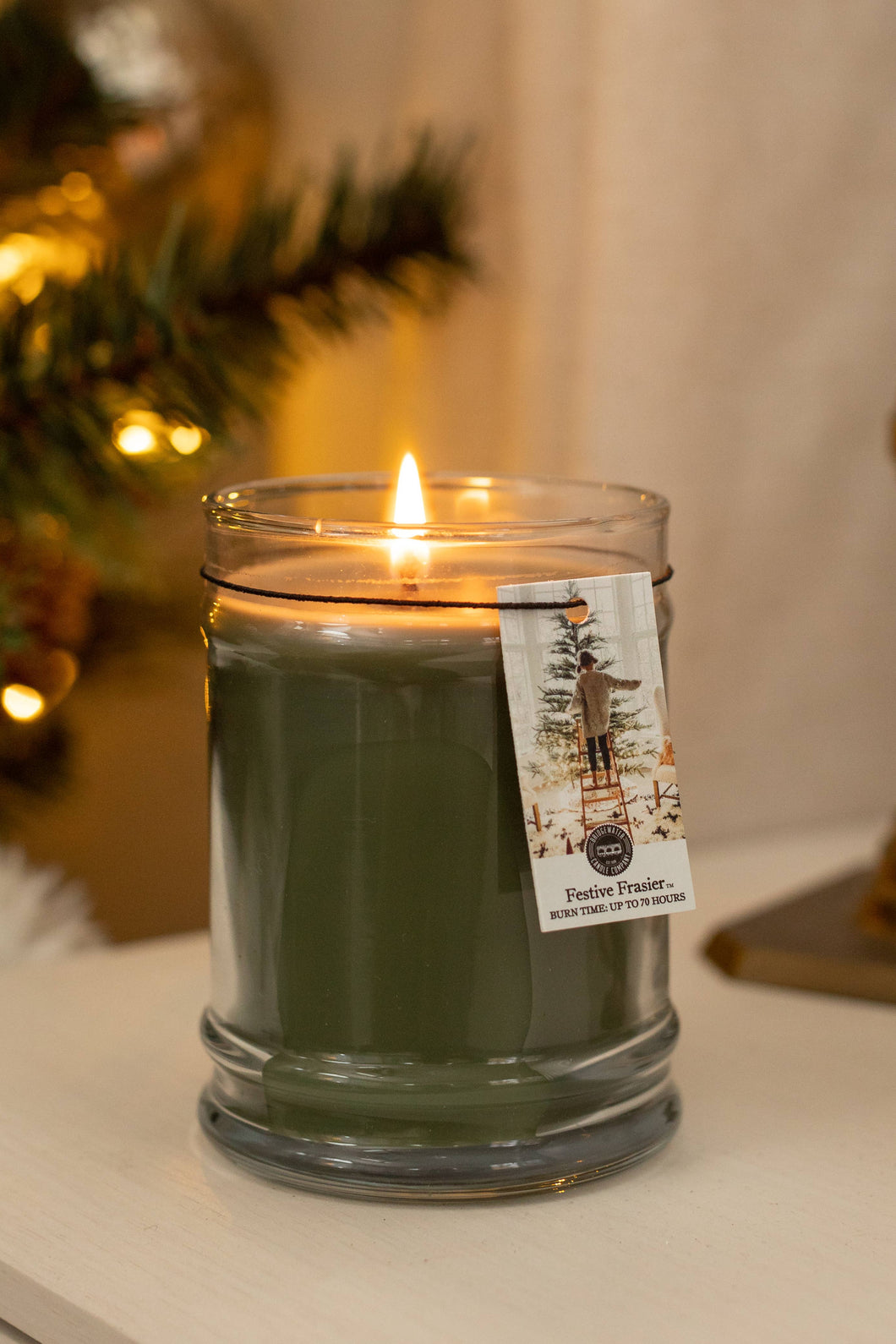 Green candle with a label on a surface, with a blurred background of lights and decor.