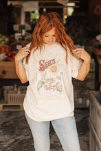 Load image into Gallery viewer, Woman wearing a &#39;Seeds&#39; t-shirt in an indoor setting with produce in the background
