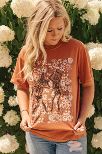 Woman wearing a rust-colored t-shirt with skeleton design in front of white flowers