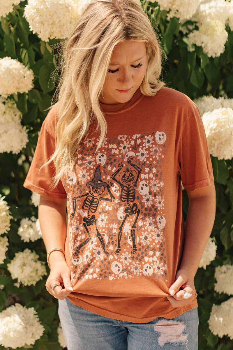 Woman wearing a rust-colored t-shirt with skeleton design in front of white flowers