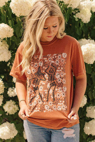 Woman wearing a rust-colored t-shirt with skeleton design in front of white flowers