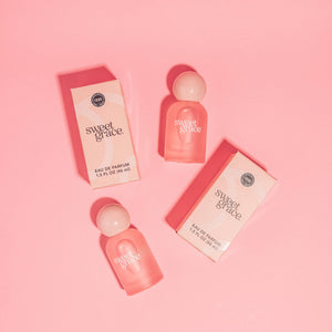 Two 'sweet grace' perfume bottles and their packaging on a pink background
