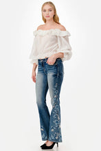 Load image into Gallery viewer, Woman wearing a white off-shoulder top and blue jeans with floral embroidery on a white background