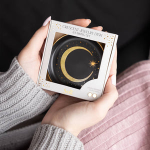 Person holding a box of a crescent jewelry dish against a dark background
