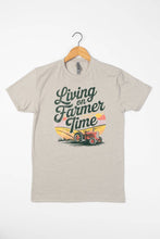 Load image into Gallery viewer, Beige t-shirt with 'Living on Farmer Time' graphic on a hanger against a white background