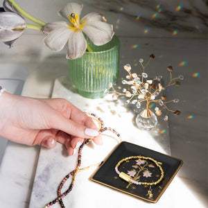 Person holding a beaded necklace with a decorative tray featuring a floral design on a marble surface.