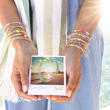 Load image into Gallery viewer, Person wearing colorful bracelets holding a Scout bracelet card with a beach scene.