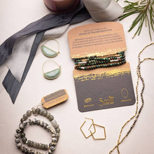 Load image into Gallery viewer, Jewelry set with bracelets, necklaces, and earrings on a white surface with a gray ribbon and greenery.