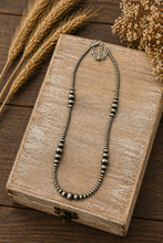 Load image into Gallery viewer, Silver beaded necklace on a wooden book with wheat stalks and dried flowers.