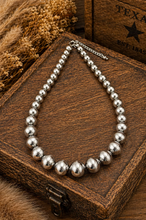 Load image into Gallery viewer, Silver beaded bracelet on a wooden box with dried flowers and a leather texture background.